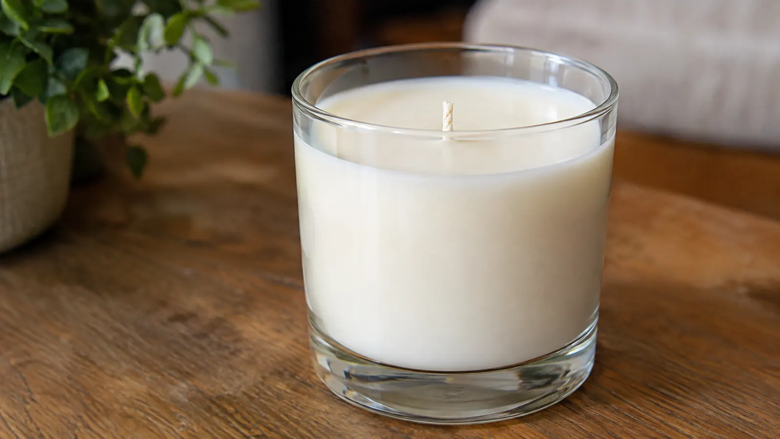 A close view of a cured soy candle with a smooth cream colored top and a single cotton wick in a clear glass jar